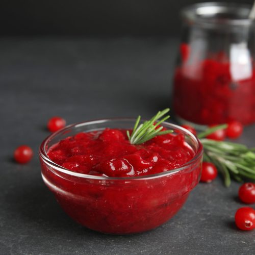 Bowl of cranberry sauce with rosemary on grey table, closeup