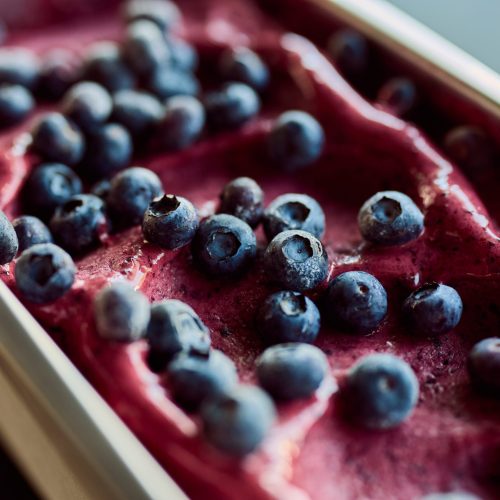 Photo of a blueberry gelato ice cream in a pink color with some fresh blueberries on top.