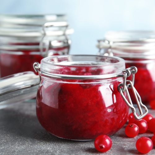 Glass jars with cranberry sauce on table, closeup