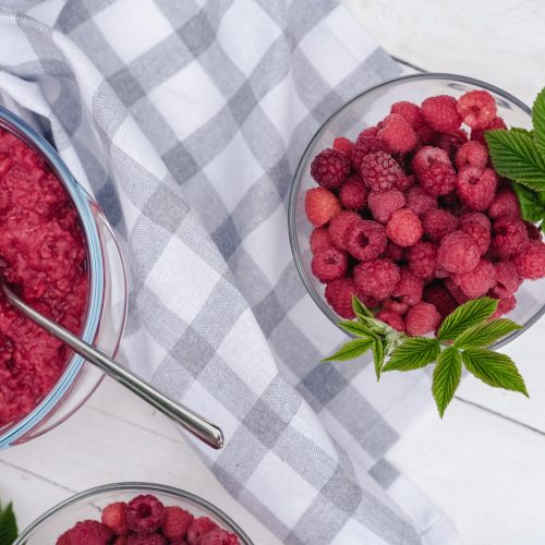 raspberry jam making. berries and leaves on the table with ready raspberry jam and spoons. summer canned berries. harvesting concept. close up view