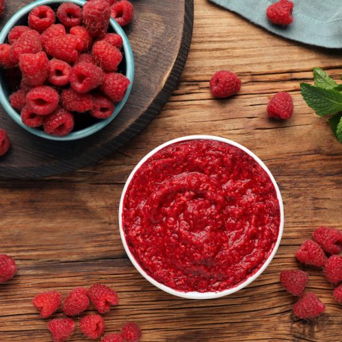 Raspberry puree in bowl and fresh berries on wooden table, flat lay