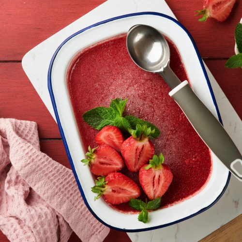 Strawberry granita or fresh berry sorbet in white rustic bowl on old wooden table background. Ice cream with strawberry and mint. Summer treat. Top view.