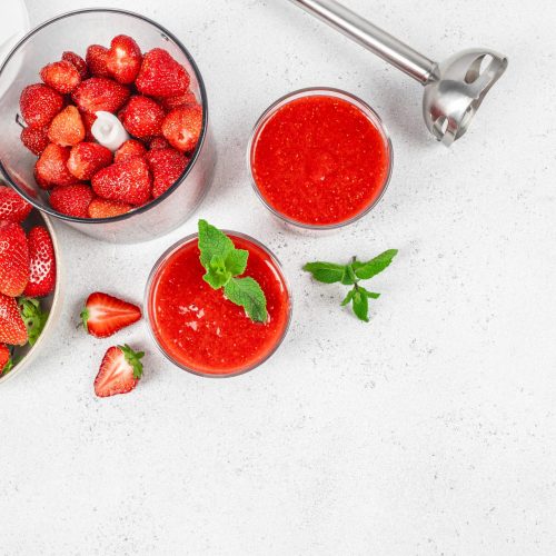 Strawberry puree preparation with fresh berries and blender on a white kitchen background, ready for recipe use. top view. copy space.