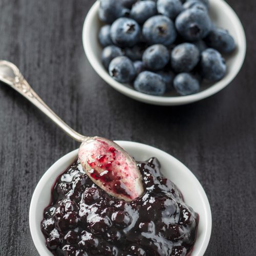 Sweet blueberry jam and blueberries on black table.